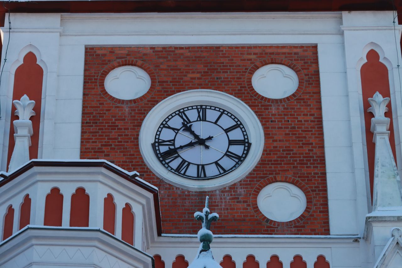 our-story Close-up of a historical brick facade featuring a large black and white clock with Roman numerals.
