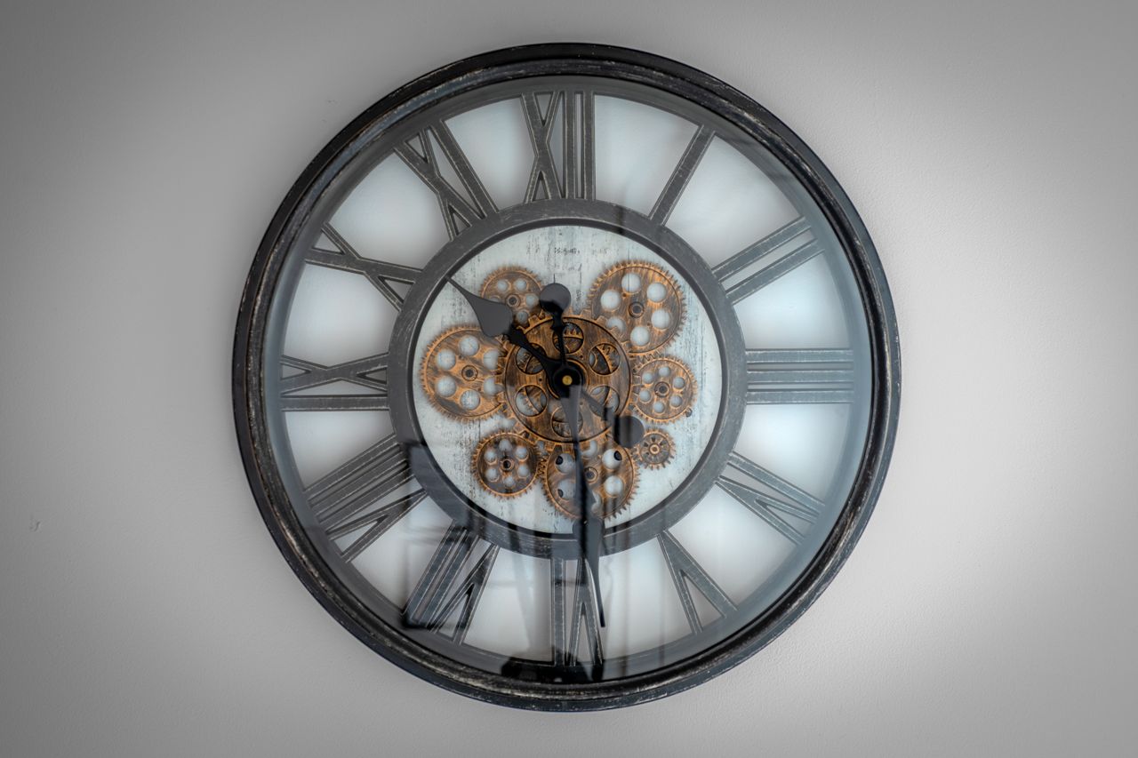 Close-up of a vintage Roman numeral wall clock with visible gears and metal frame.
