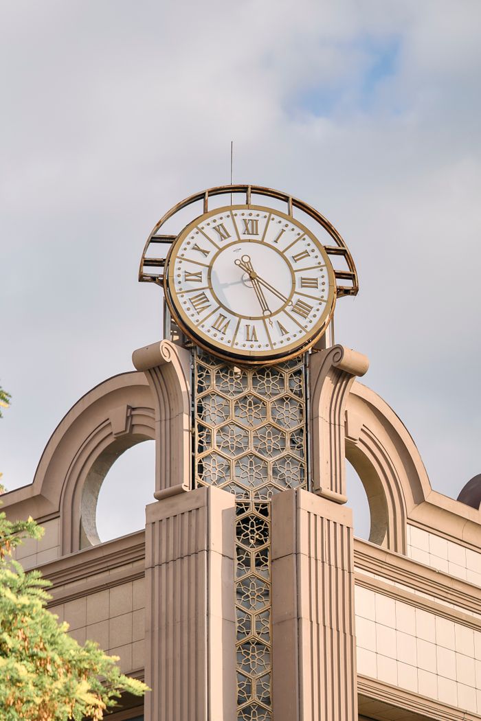 who-we-are A classic architectural clock tower with Roman numerals and intricate details under a bright blue sky.