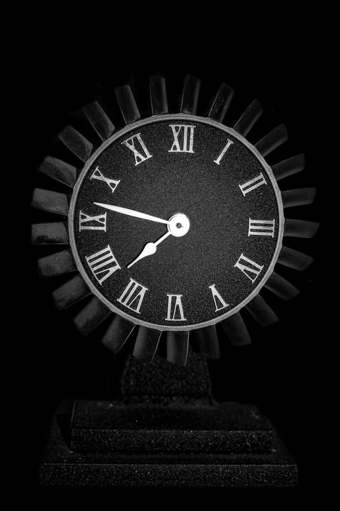 Stylish black clock with Roman numerals against a dark background.