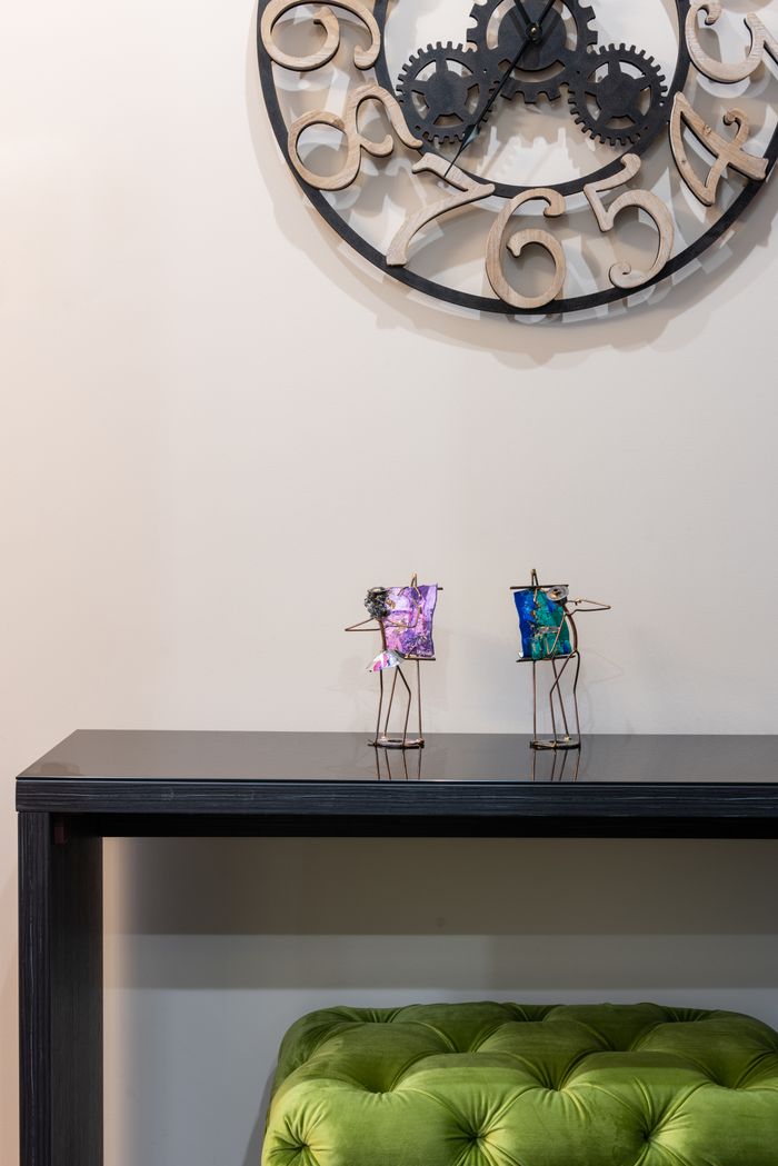 Green soft pouf placed at black table with souvenirs placed near white wall with round decorative clock in light room